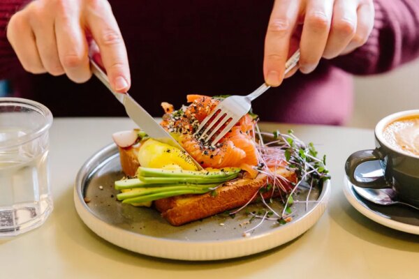 A man's hands cutting a salmon and avocado flatbread with a knife and fork.