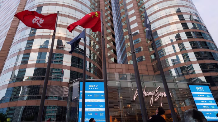 Hong Kong and China flags fly next to electronic boards displaying Hang Seng Index prices outside Exchange Square in Hong Kong.