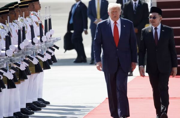 US President Donald Trump walks on a red carpet with Malaysian Prime Minister Anwar Ibrahim past an honour guard.