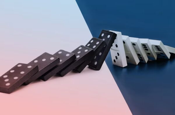 Black and white dominoes falling in a row on a surface divided between pink and blue backgrounds.
