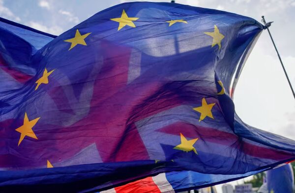 A European Union flag waves in front of a Union Jack flag outside the Houses of Parliament in London.