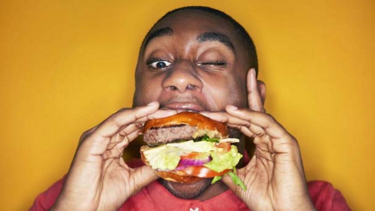An overweight girl standing on scales and holding her left hand up to her head looking sad - while wearing a brown and white polka dot dress.