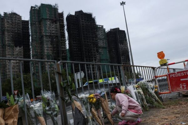 A girl places flowers in front of the fire-damaged residential blocks at Wang Fuk Court. Pic: Reuters