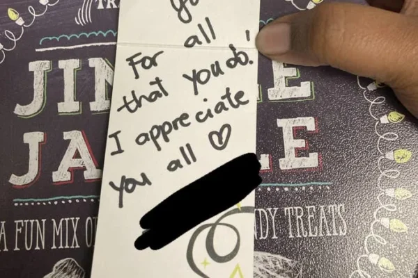 A thank you note atop a tin of snacks reads: "Thank you for all that you do! I appreciate you all" with a heart symbol