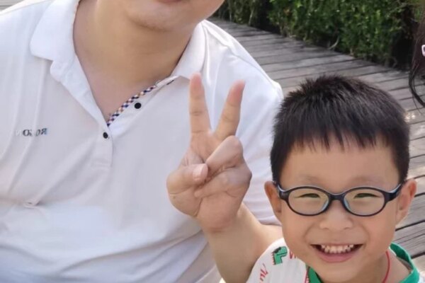 Fei Zhang poses with a peace sign next to his son, Yuanxin, while seated together outside