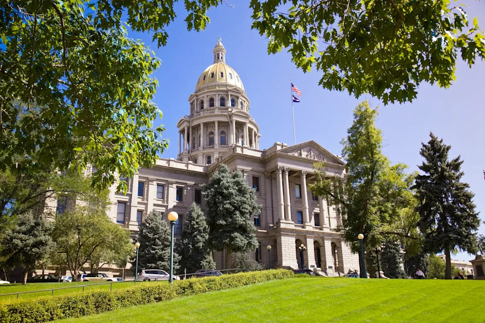 A large building with a gold dome on a sunny day behind a green lawn.