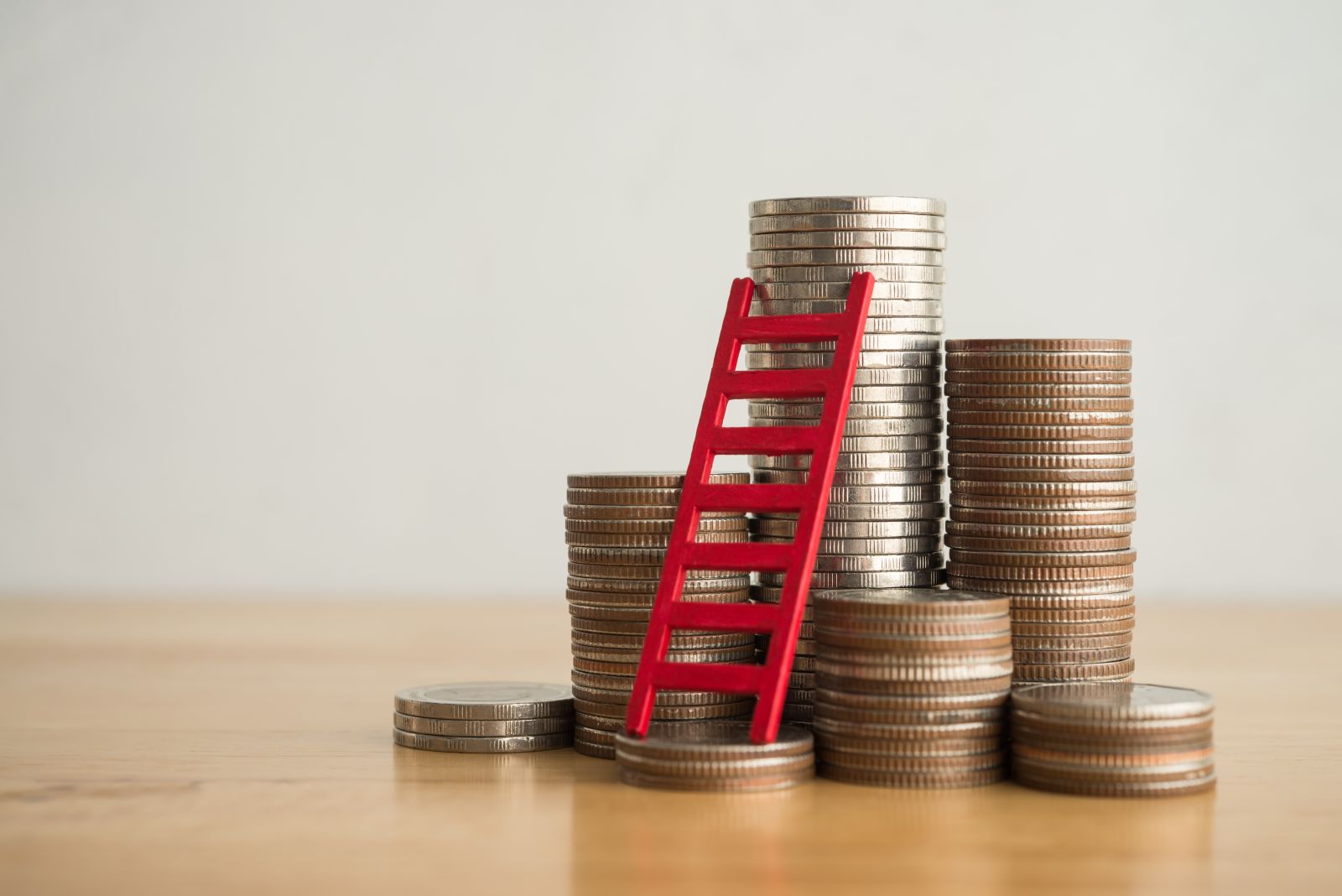 A concept image showing a red ladder next to stacks of coins by Pla2na via Shutterstock