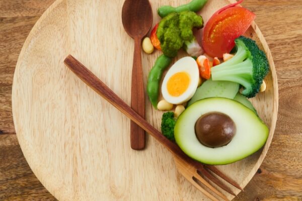 Food on a wooden plate in one section with cutlery placed to like hands on a clock