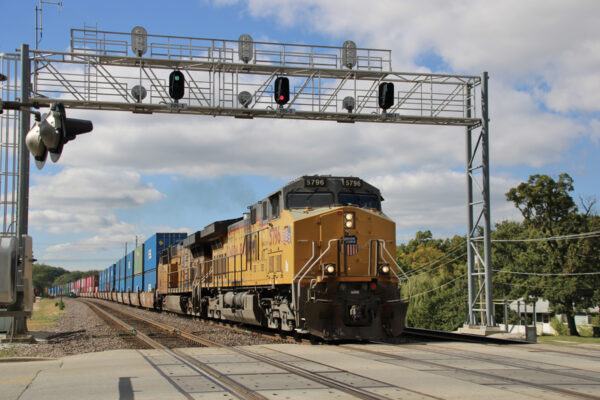 Freight train with two yellow locomotives passing under signal bridge