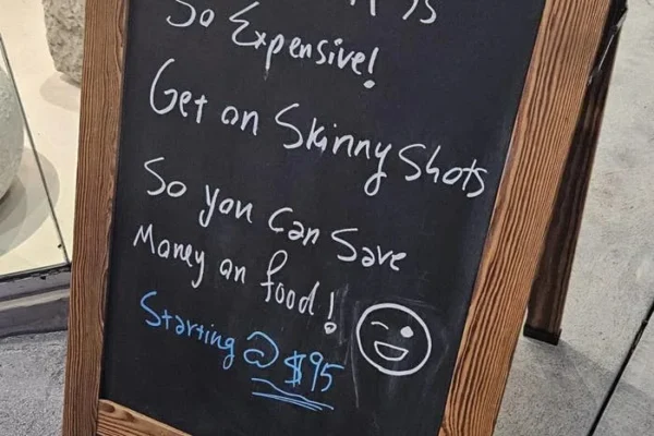 Chalkboard sign promoting "Skinny Shots" at $75, suggesting they help save money on food by losing weight