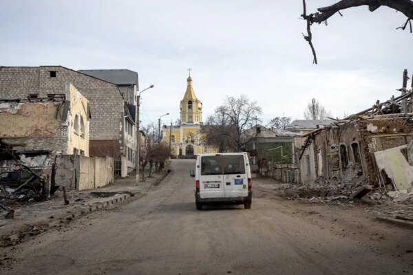 A lone evacuation vehicle travels along a damaged street in a heavily ruined Ukrainian city.