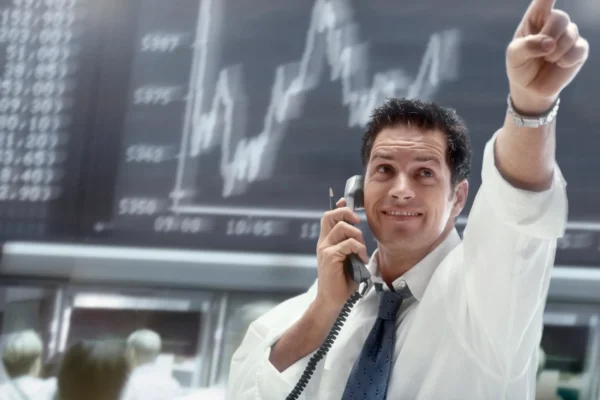 A person on the phone pointing to movement on a stock chart.