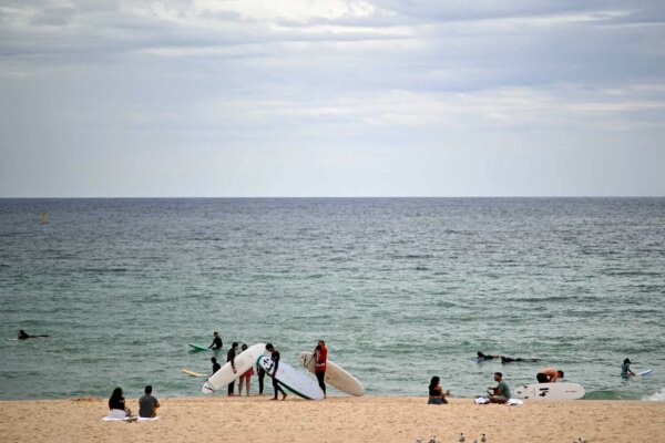 people with surfboards stand on a beach with the ocean behind them.