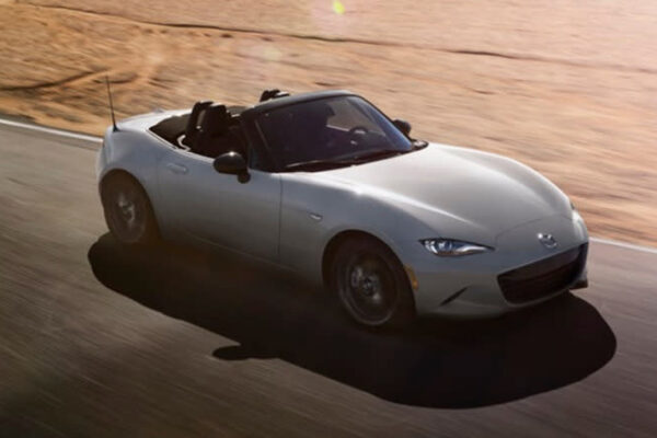 A 2024 Mazda MX-5 Miata with its roof down driving on a road