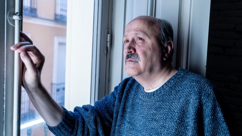 Senior man in his 60s feeling desperate sad looking throughout the balcony worried depressed thoughtful and lonely at home in Aging Depression