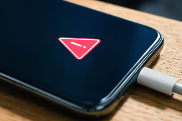 A phone sitting on a table, plugged in, with a warning logo on the screen