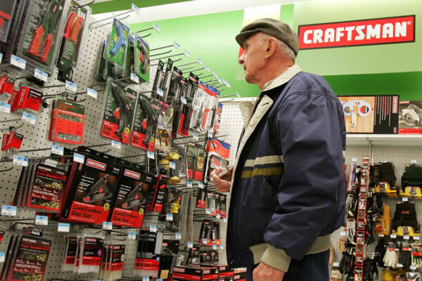 An older adult in a flat cap looks at Craftsman tools hanging on a display in a hardware store.