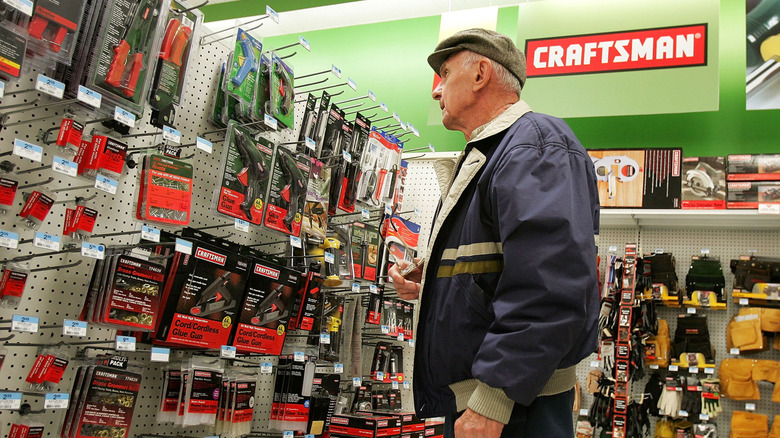 An older adult in a flat cap looks at Craftsman tools hanging on a display in a hardware store.