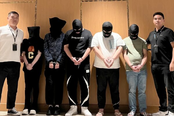 Police officers escort detained men during a custody transfer at an airport.