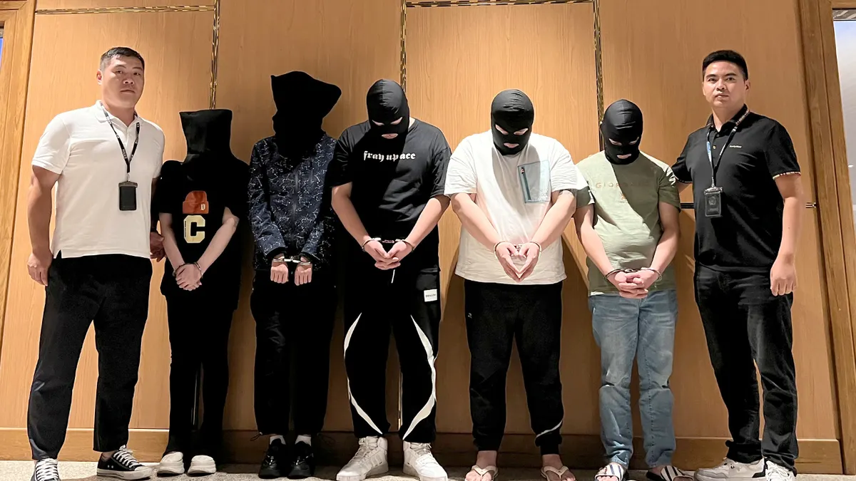 Police officers escort detained men during a custody transfer at an airport.