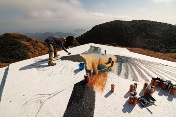 Rob Aspire paints a Long-tailed Shrike on the rooftop of a stone house on Sunset Peak, Lantau, Hong Kong on Jan. 25, 2025. (AP Photo/May James)