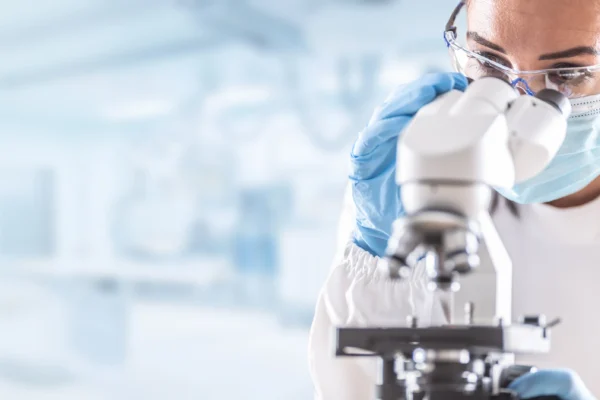 Person in a lab gazing into a microscope.