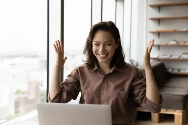 An investor cheers behind a laptop at home.