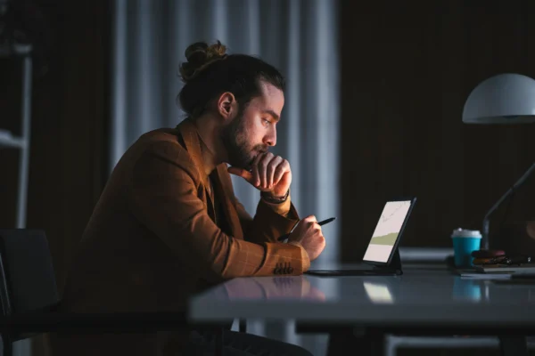 An investor studies something on a laptop in a darkened office.