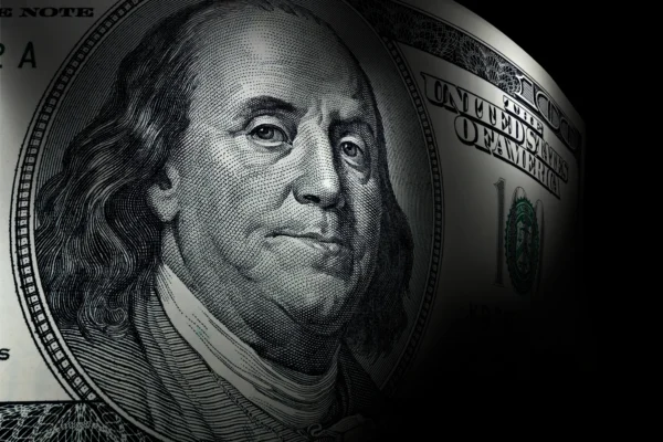 An up-close view of Benjamin Franklin's portrait on a hundred dollar bill, surrounded by a dark background.