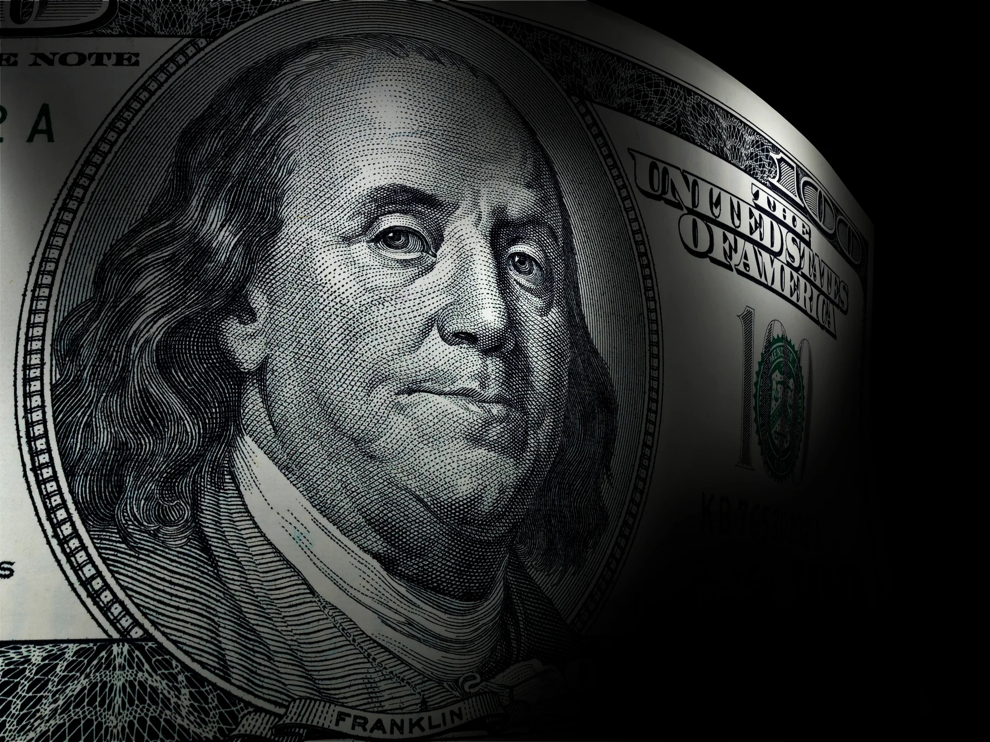 An up-close view of Benjamin Franklin's portrait on a hundred dollar bill, surrounded by a dark background.
