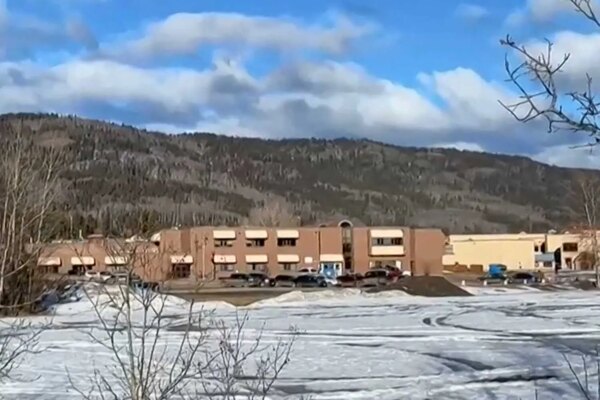 A school building with cars and snow out front. There are hills in the background.
