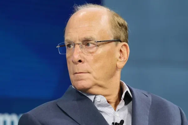 Larry Fink sits on stage in a blue suit and dress shirt, looking sharply over his right shoulder.