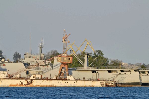 Ships docked in a port, with trees behind them.