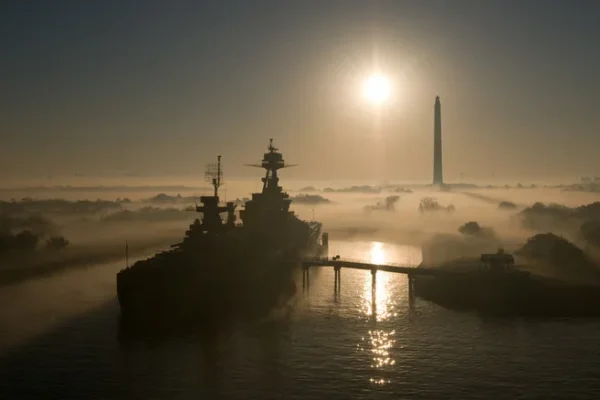 Battleship USS Texas seen from a high distance front port side view in morning fog with San Jacinto Monument in background
