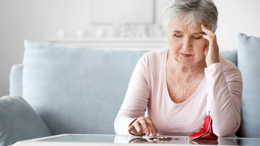 Sad senior woman counting money at home