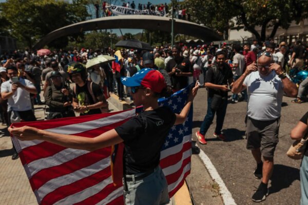 A person in a red-and-blue cap holds a large American flag. A crowd fills the background.