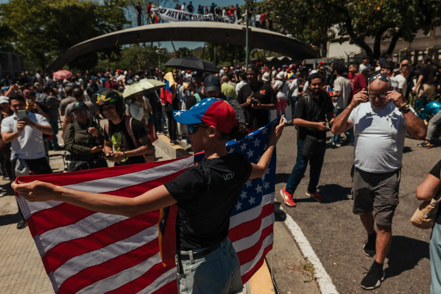 A person in a red-and-blue cap holds a large American flag. A crowd fills the background.
