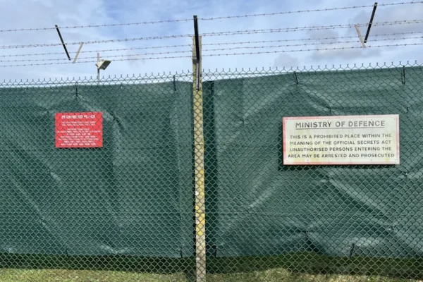 Green tarpaulin attached to a chain link fence with barbed wire running across the top