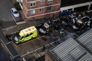 An aerial photograph showing three blackened and burned out ambulances and one badly damaged one, parked outside a building.