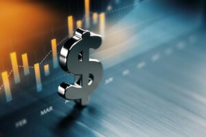 A photo illustration shows a silver 3-dimensional dollar sign sitting on a blue surface with a chart of bars in orange behind it.