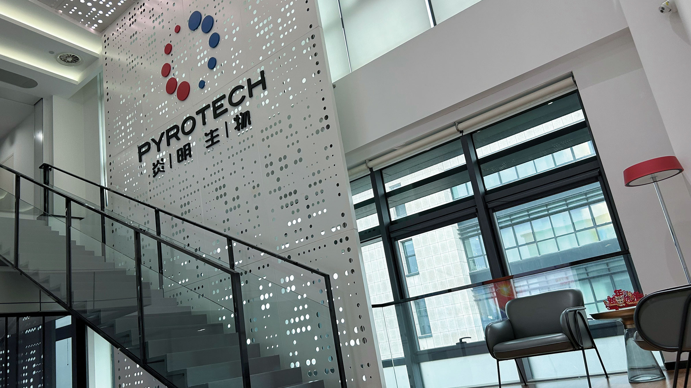 A two-story interior with many windows features a mural with the word “Pyrotech” and a logo of 10 circles arranged in a circle.