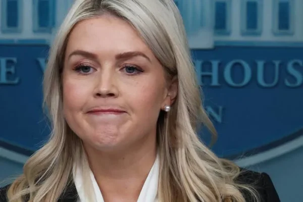 A person stands at a podium in front of a White House backdrop, appearing focused and thoughtful during a press briefing