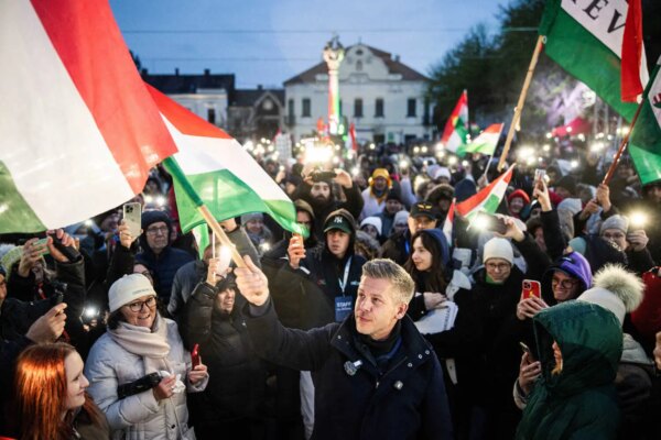Peter Magyar stands at the head of a large crowd of people, many holding Hungarian flags, in an outdoor setting with buildings in the background.