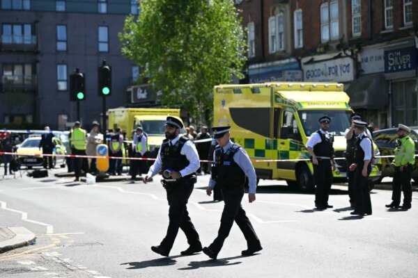 A street scene shows uniformed police officers and yellow ambulances behind police tape.