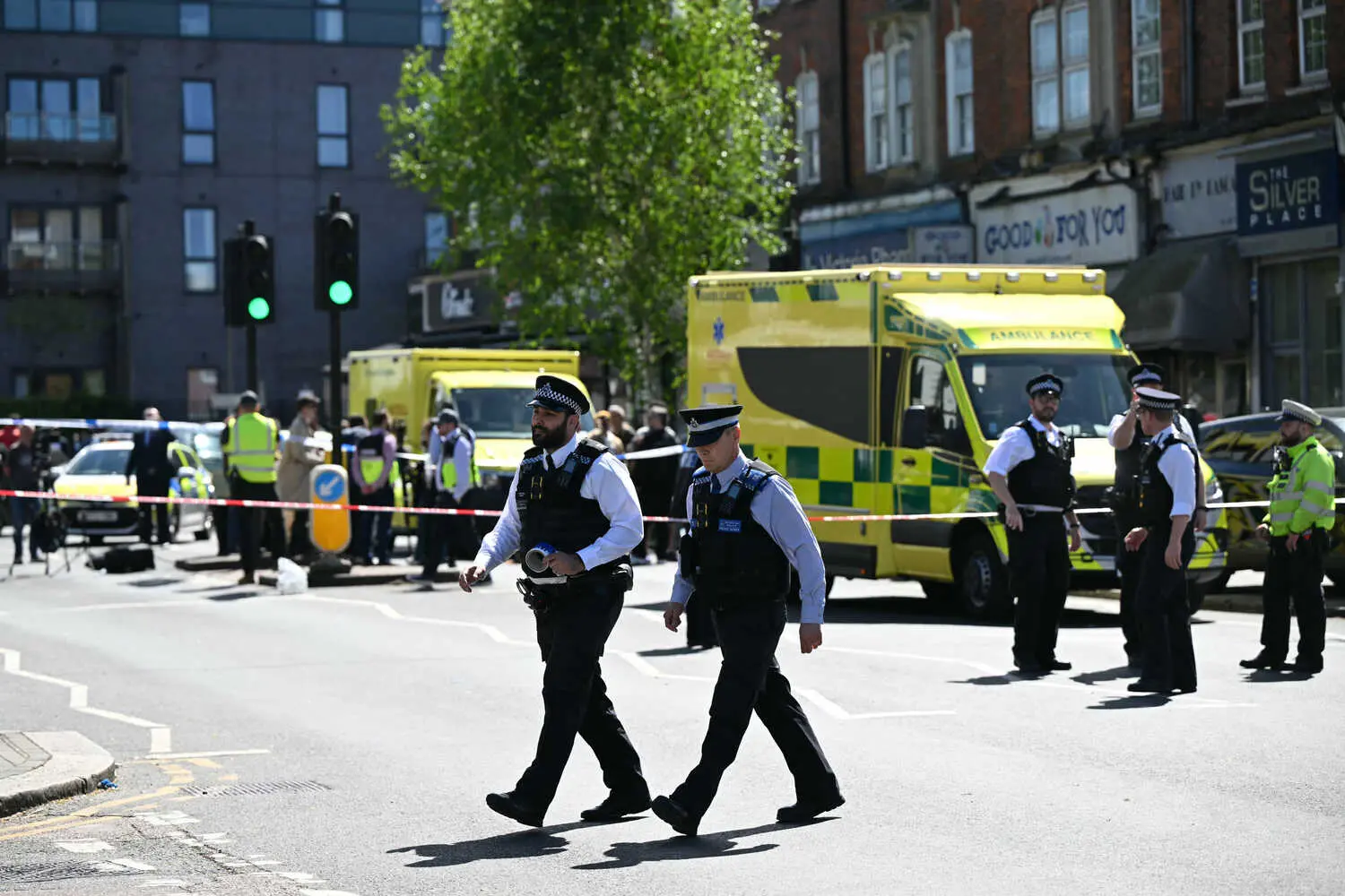 A street scene shows uniformed police officers and yellow ambulances behind police tape.