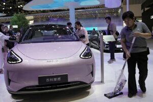 A staff member cleans the floor next to a Geely GEOME Xingyuan electric vehicle (EV), also known as Geely EX2, displayed at the Beijing International Automotive Exhibition, or Auto China, in Beijing, China April 26, 2026.