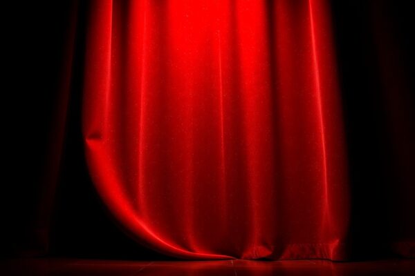 An extreme close-up photograph of luxurious, shimmering red velvet fabric in dramatic studio lighting, conceptually representing the glamour and prestige of a national performing arts center.