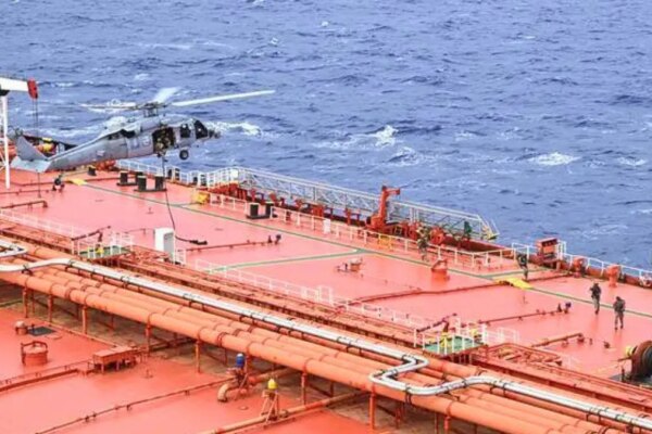 A white U.S. military helicopter hovers over the bright orange sanctioned stateless crude oil tanker M/T Tifani during an U.S. interdiction.