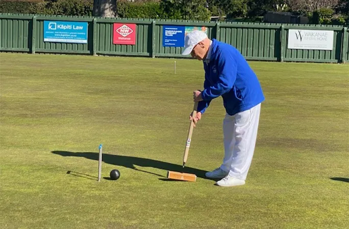 101-year-old Neville Sandiford in a white hat and blue jacket playing croquet on a green lawn.