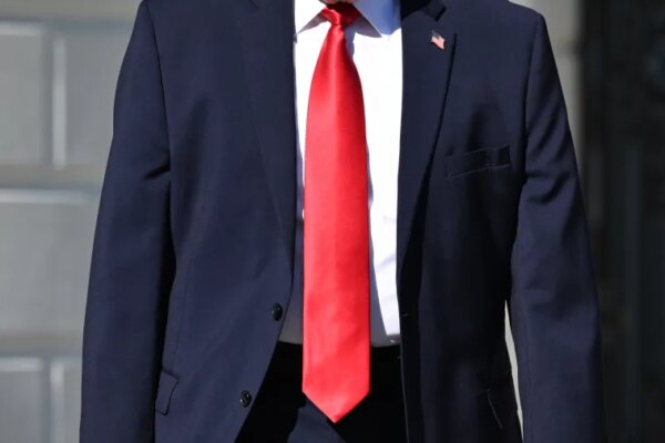 Donald Trump in a navy suit and red tie walking outdoors.
